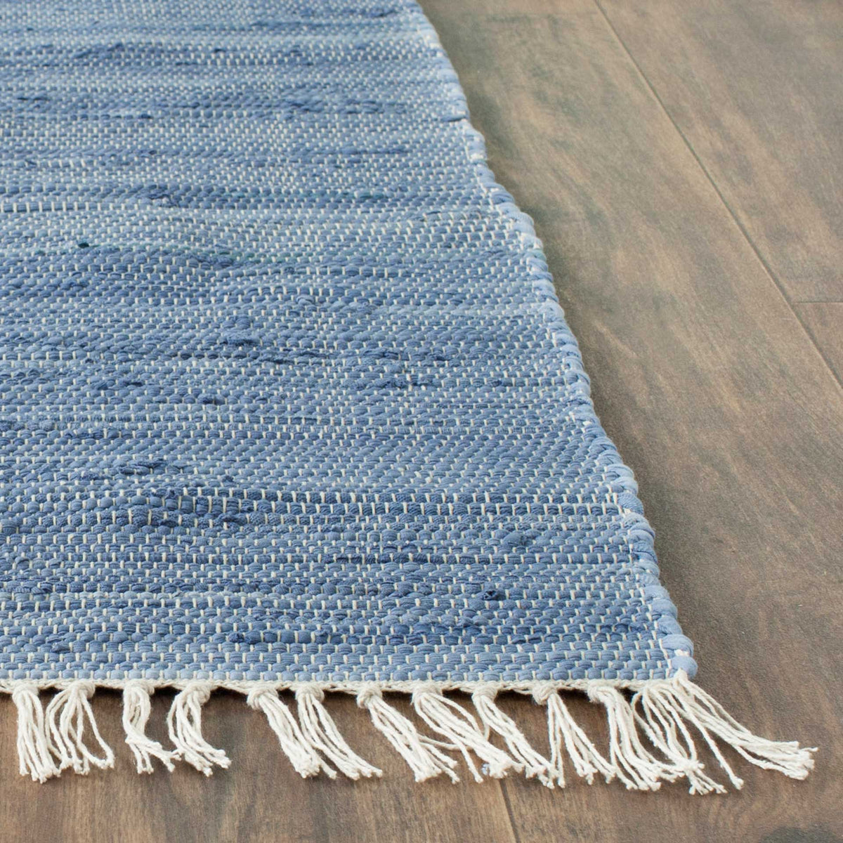 Cream fringe trims the corner of a blue handwoven cotton rug, revealing its tightly textured weave.