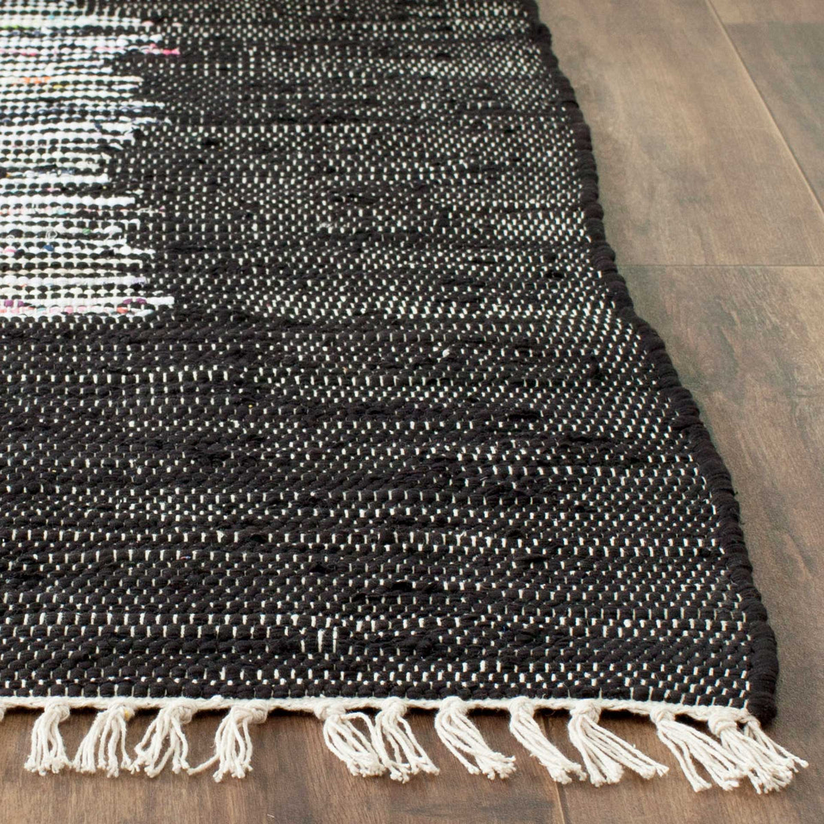 Ivory tassels soften the corner of a richly textured black cotton rug with subtle ivory threads.