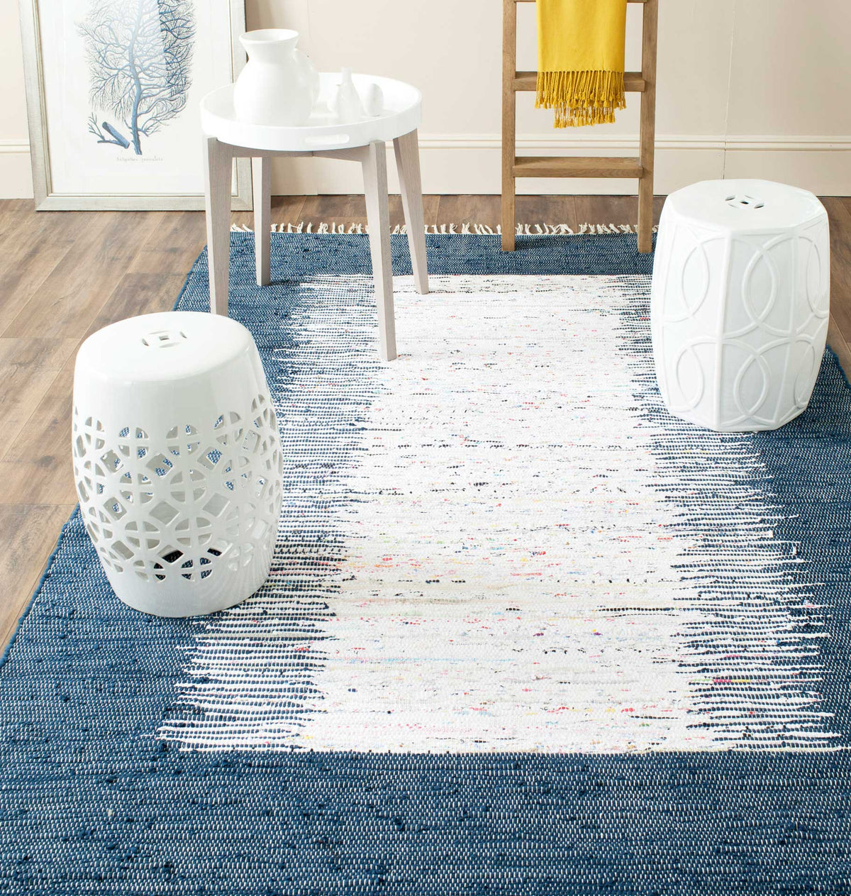 A navy and ivory woven rug grounds a bright living area beneath light wood and white accent furniture.