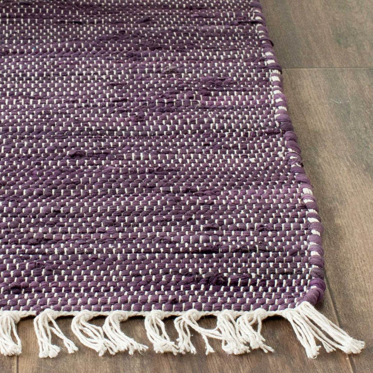 Cream tassels edge a deep purple cotton rug, revealing an intricate, nubby handwoven texture.