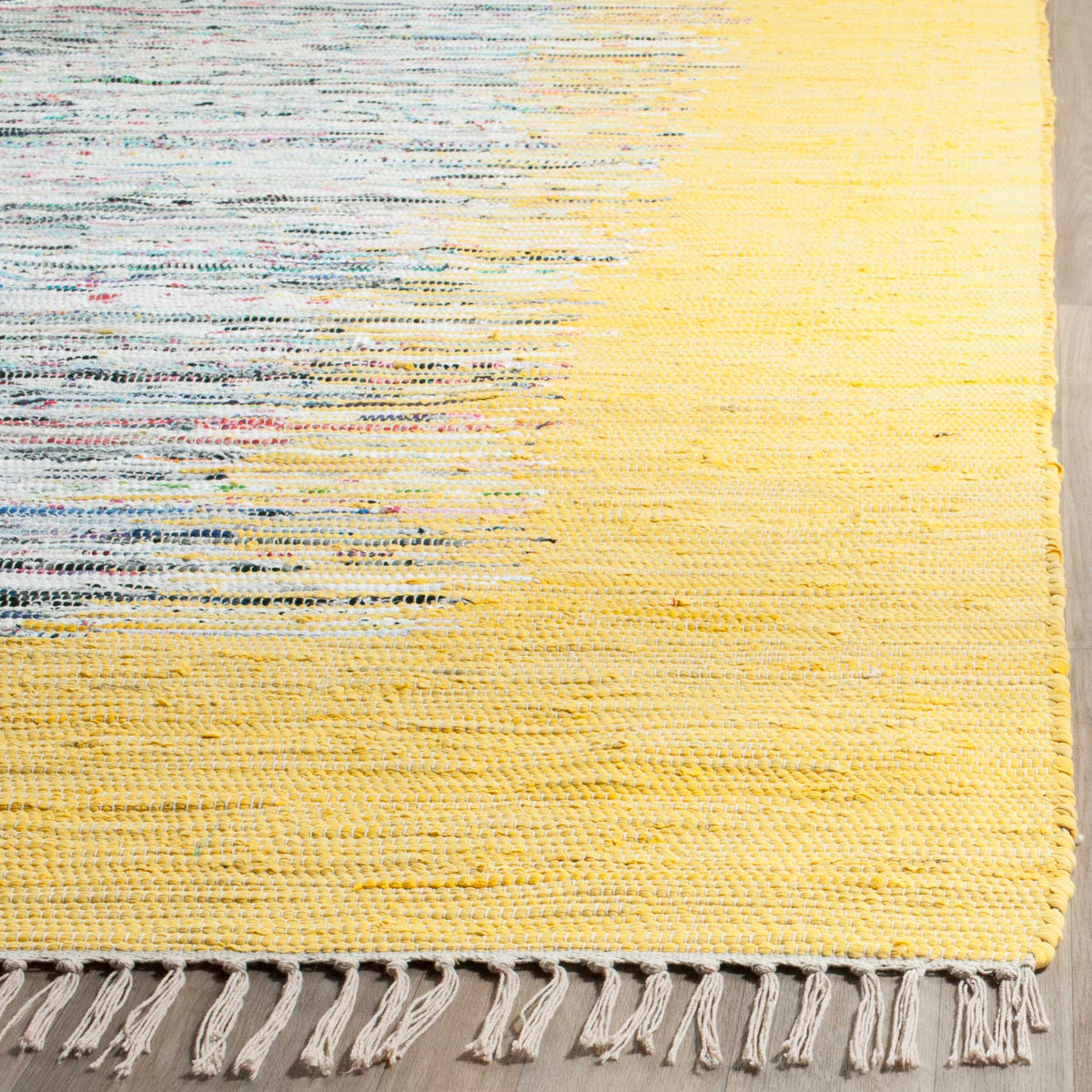 Pale fringe lines the corner of a sunny yellow cotton rug, with colorful threads woven through ivory.