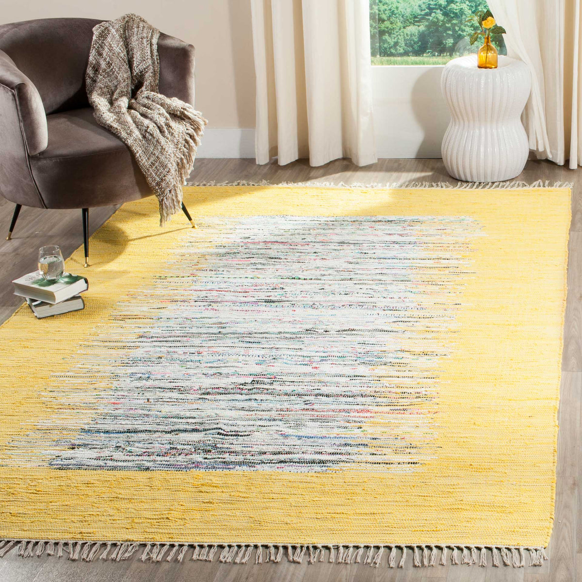 A bright yellow and ivory rug adds handwoven warmth beneath a curved chair and a white accent table.
