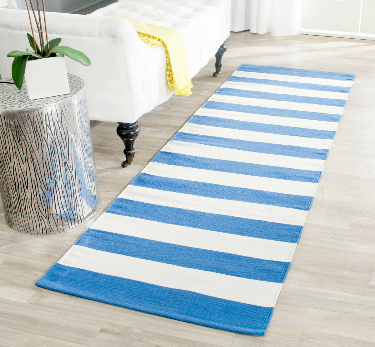 Vivid blue and ivory stripes brighten the floor beside a white upholstered bed.