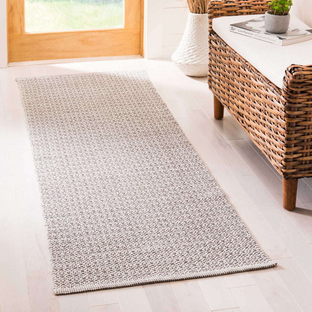 Soft ivory and gray motifs bring subtle woven texture to a runner beside natural wicker furnishings.