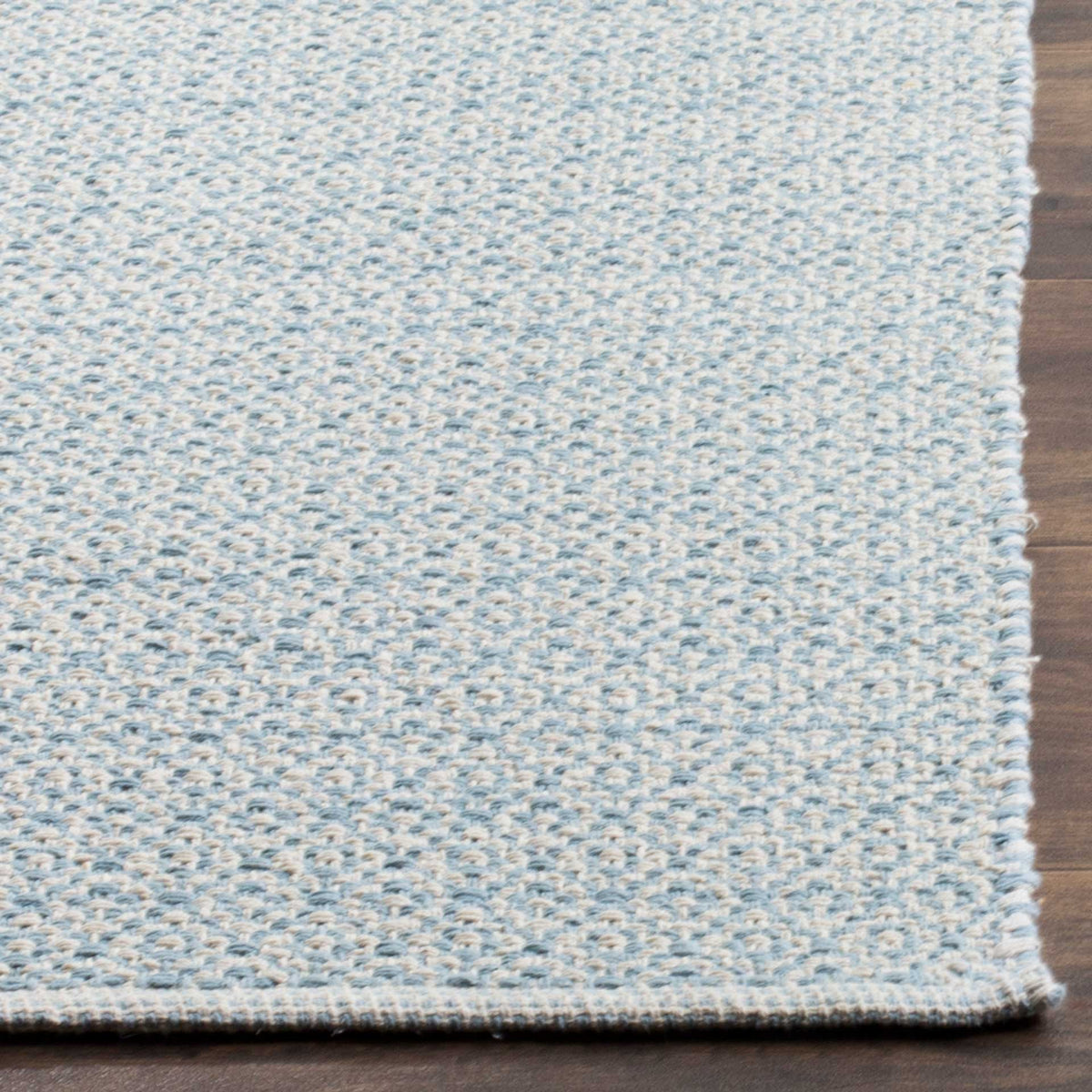 Pale blue and ivory weaving meets a tidy bound edge at the corner of this cotton rug.