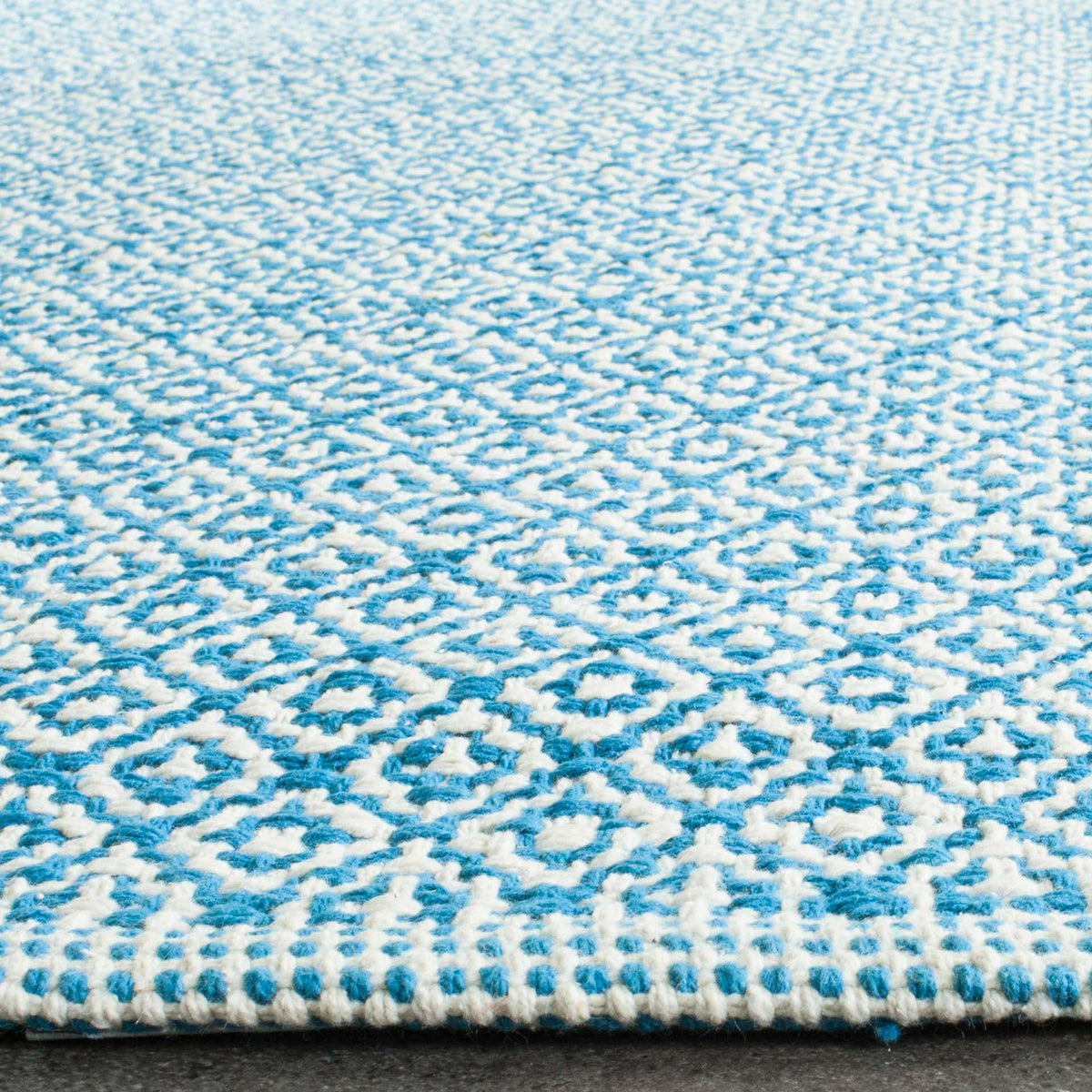 Textured ivory loops trace repeating blue diamonds above a neatly bound rug edge.