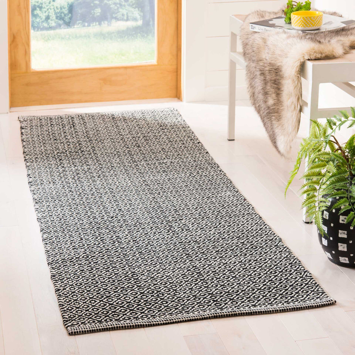 A black and ivory runner adds intricate woven pattern and bold contrast beside a sunlit doorway.