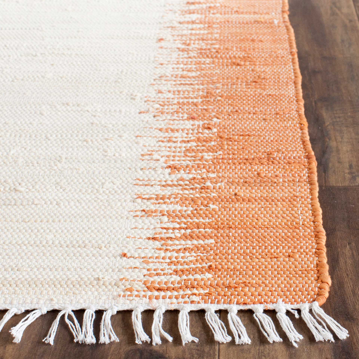 Textured orange and ivory cotton weave flows into a finished edge and loose white fringe