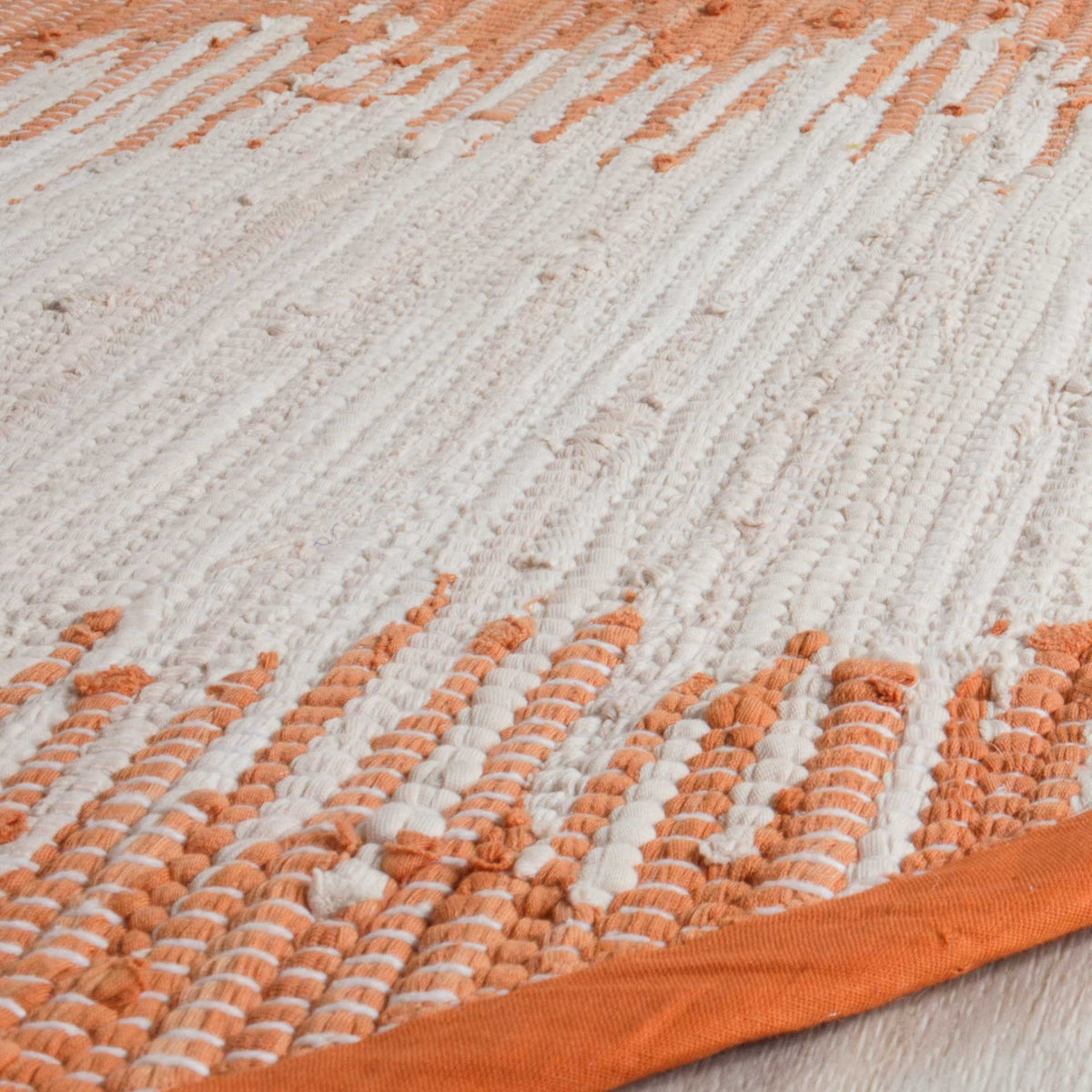 Chunky orange and ivory cotton yarns create rich texture beside a smooth orange border