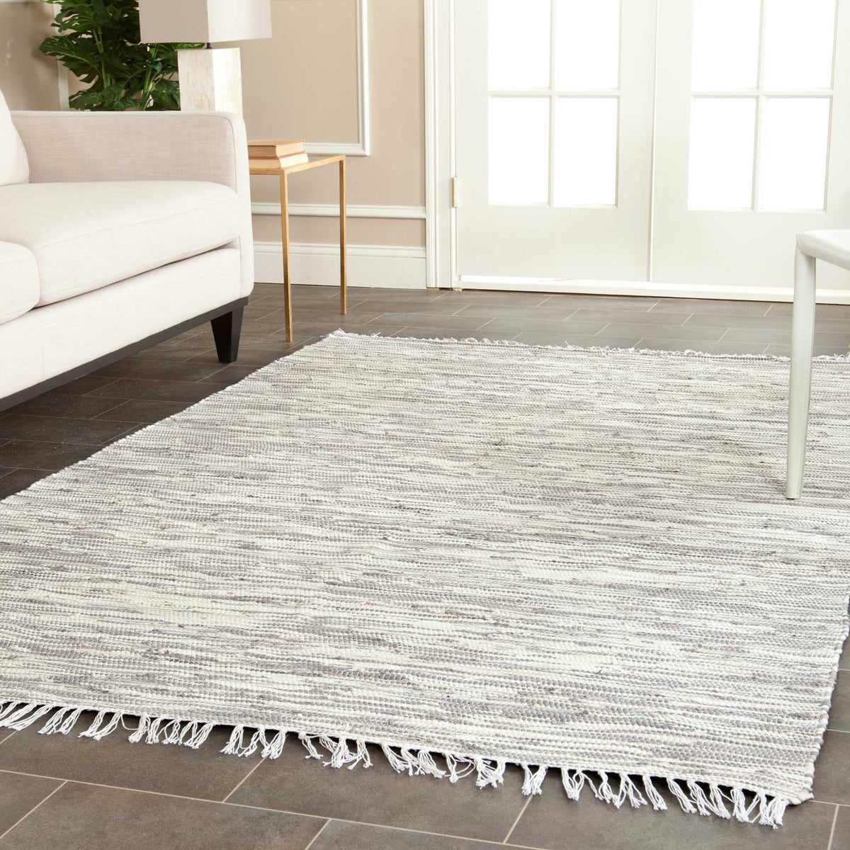Silver-gray cotton rug with rippling woven stripes and tassel fringe to ground a bright living space.