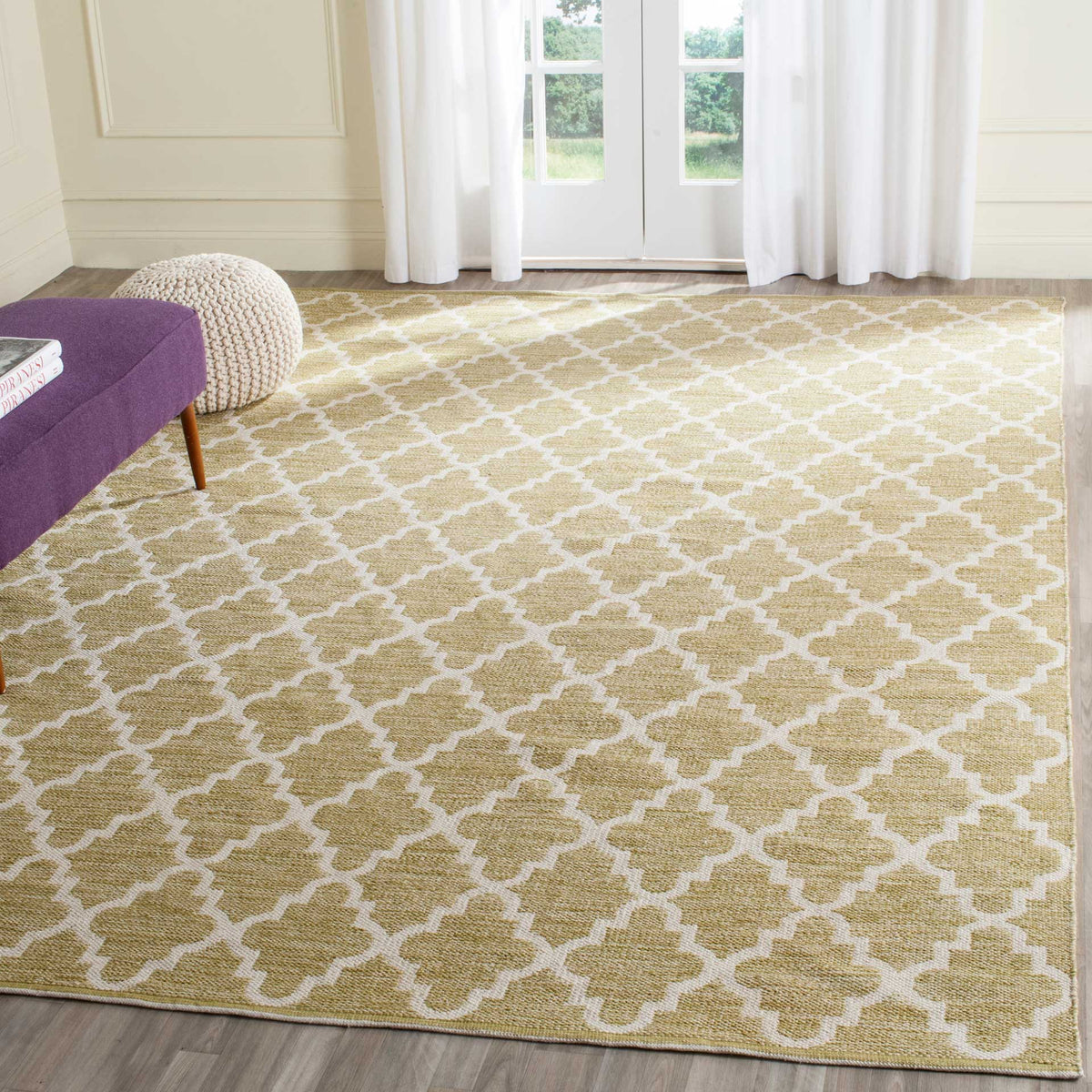 A large olive green and ivory trellis rug lends earthy warmth to a sunlit sitting area.