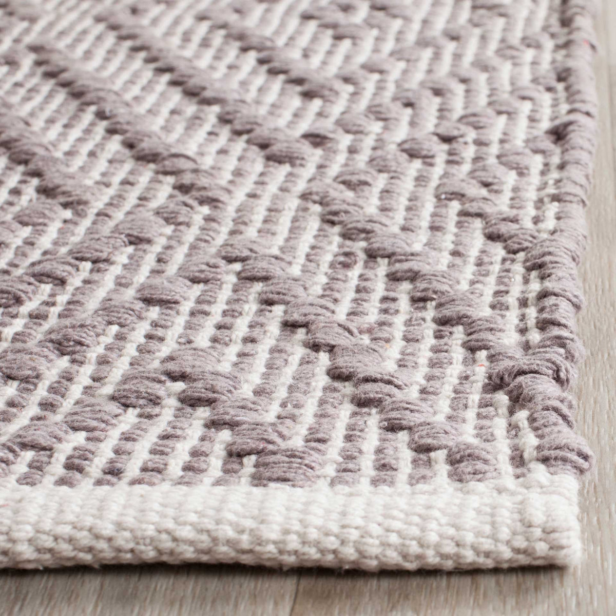 Chunky gray and ivory cotton threads meet at a thickly bound rug corner.