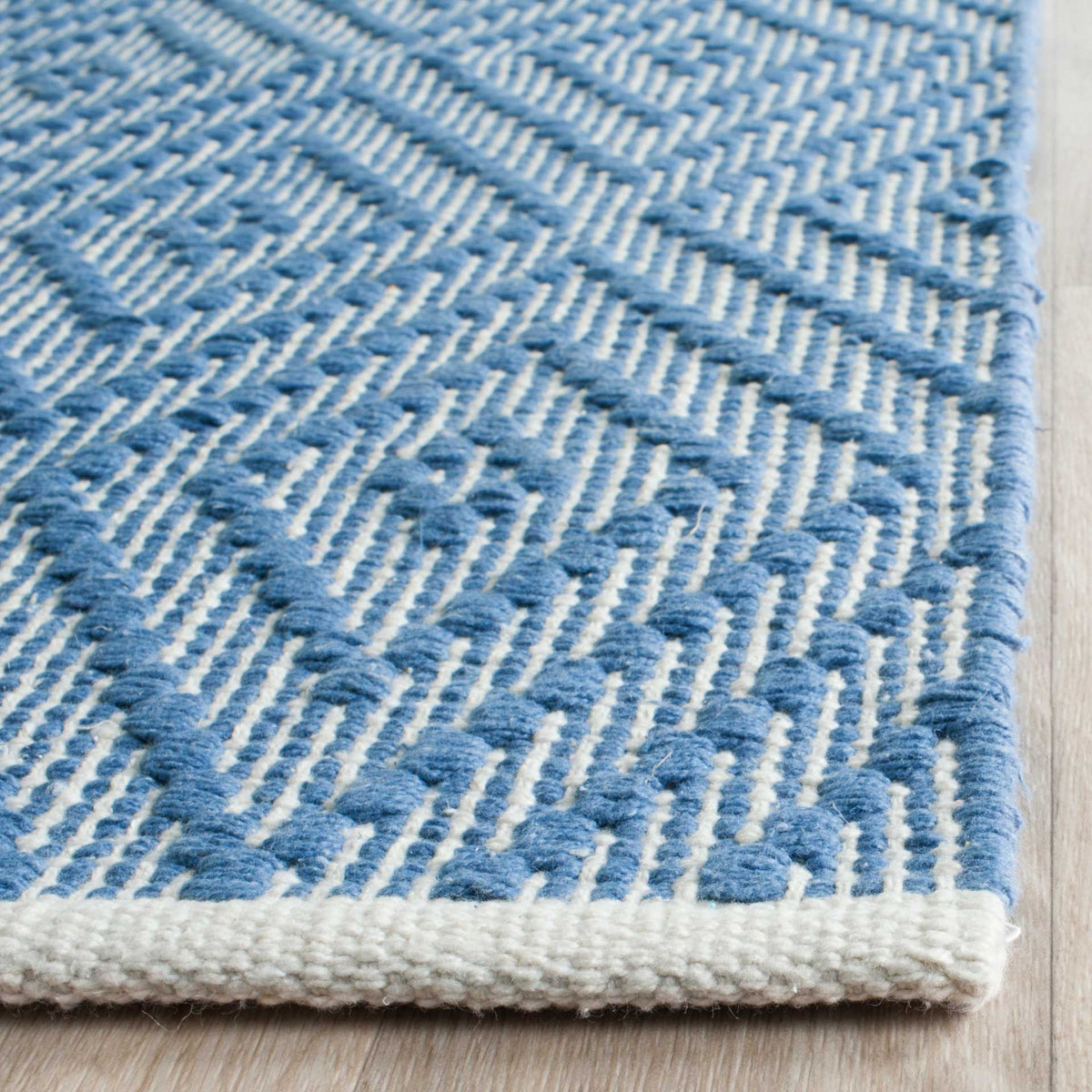 A woven ivory edge frames raised blue threads and finely patterned cotton texture.