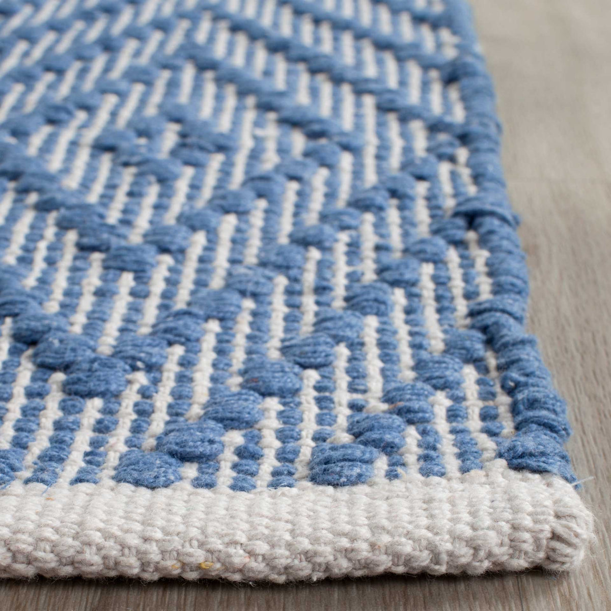 Soft blue cotton knots and an ivory binding define the textured rug corner.