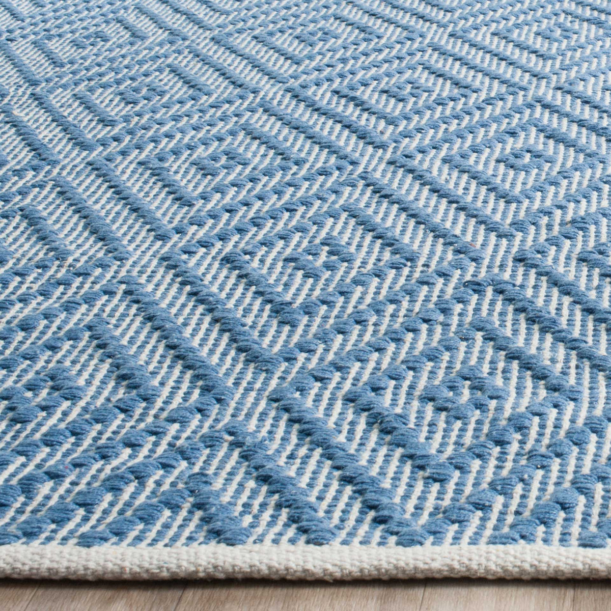 Blue woven diamonds rise from ivory cotton beside a tidy bound edge.