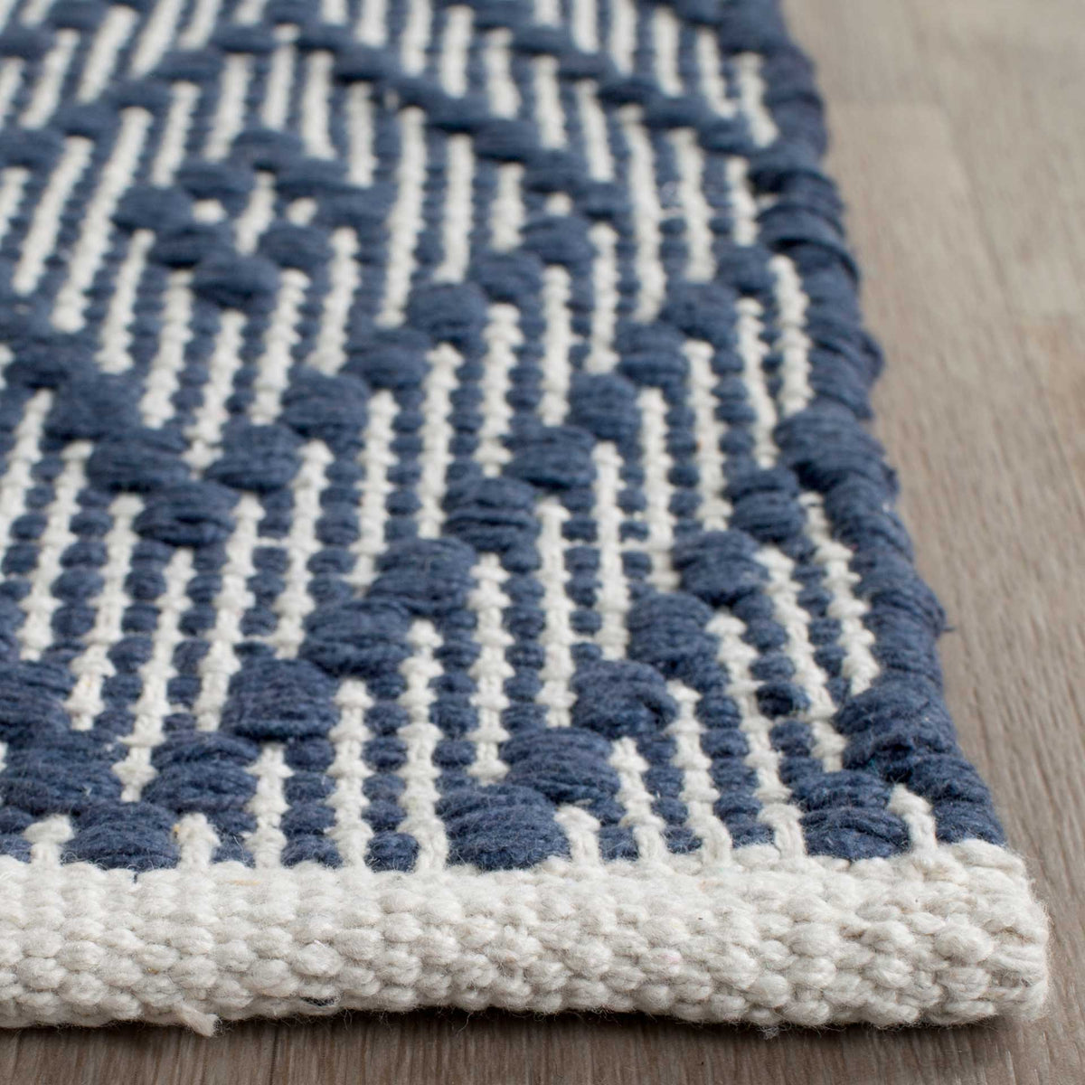 Navy and ivory woven loops show their tactile detail at a neatly bound rug corner.