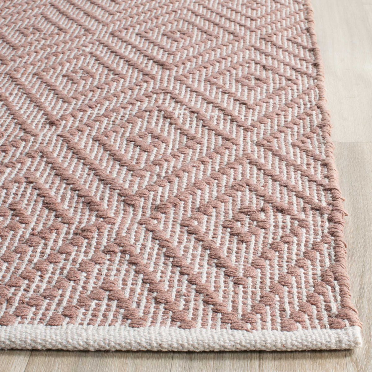 Beige and ivory cotton loops meet at a softly bound rug corner.