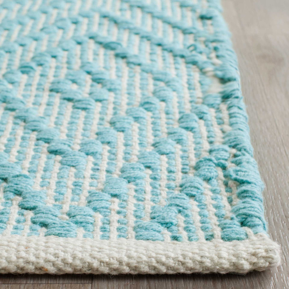 Raised turquoise knots contrast with ivory cotton at the rug's neatly finished corner.