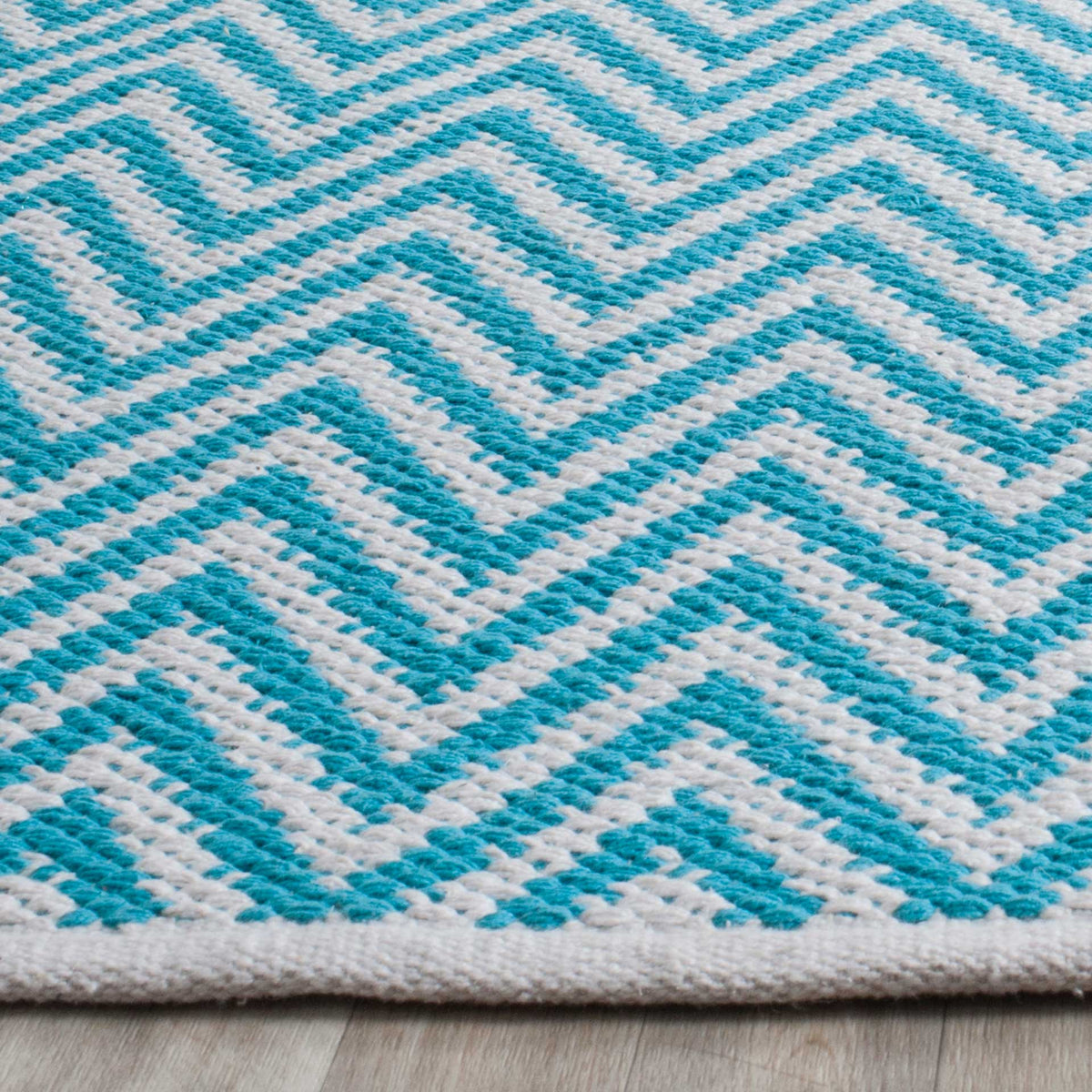 Textured turquoise cotton chevrons ripple across ivory toward a neatly finished edge.