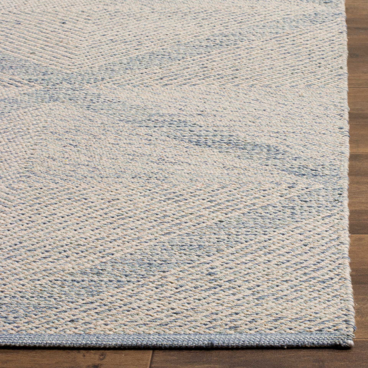A blue-bound corner frames the pale blue and ivory weave of this low-profile cotton rug.