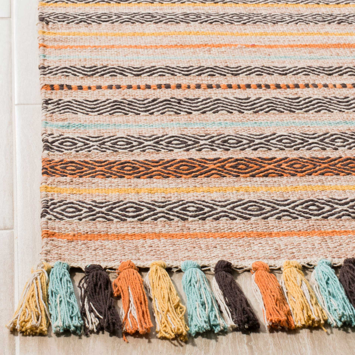 Textured beige cotton weave pairs brown geometric bands with orange, aqua, and gold tassels.