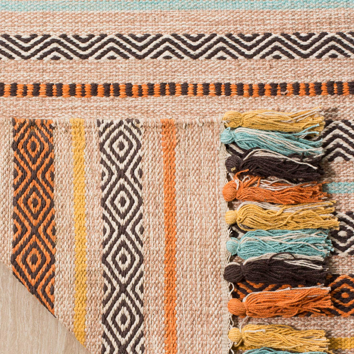 Folded beige cotton weave reveals its striped underside and bundled multicolored tassels.