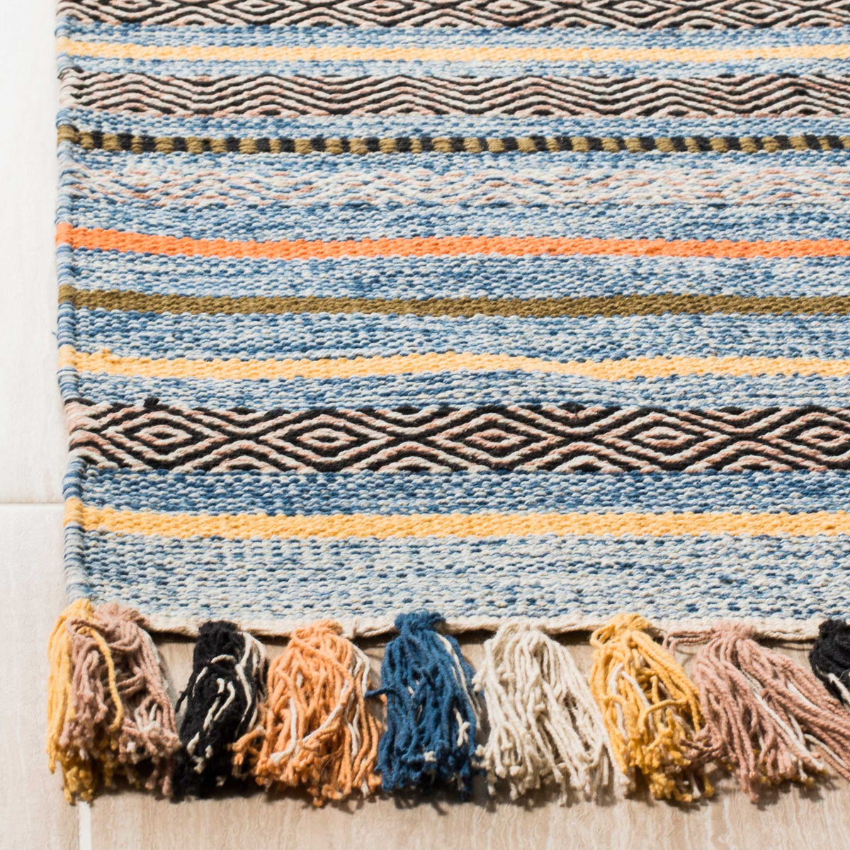 Textured blue and cream stripes frame dark woven diamonds and tassels in warm earthy colors.