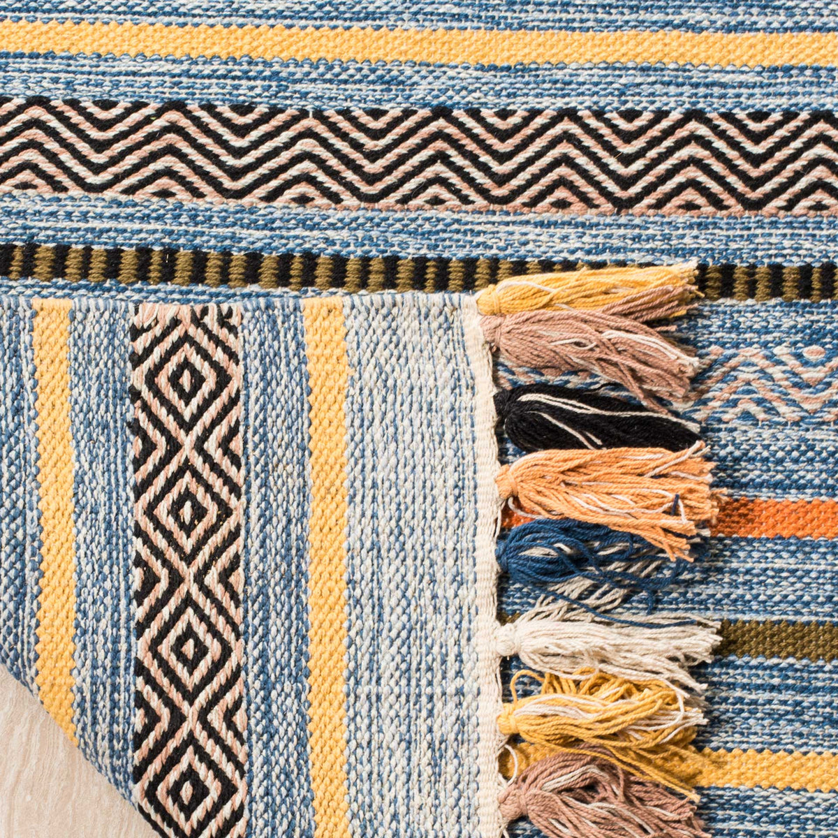 Folded cotton edge reveals woven blue stripes on the underside beside chunky multicolored tassels.