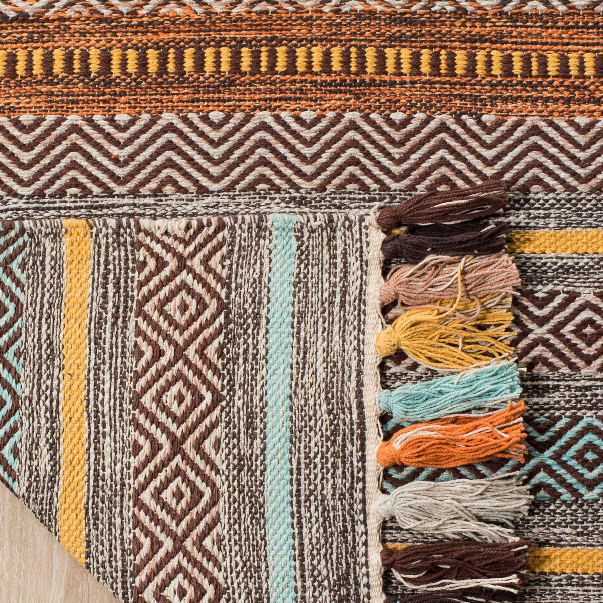 Folded rug corner shows a striped cotton underside beside bundled brown and turquoise tassels.