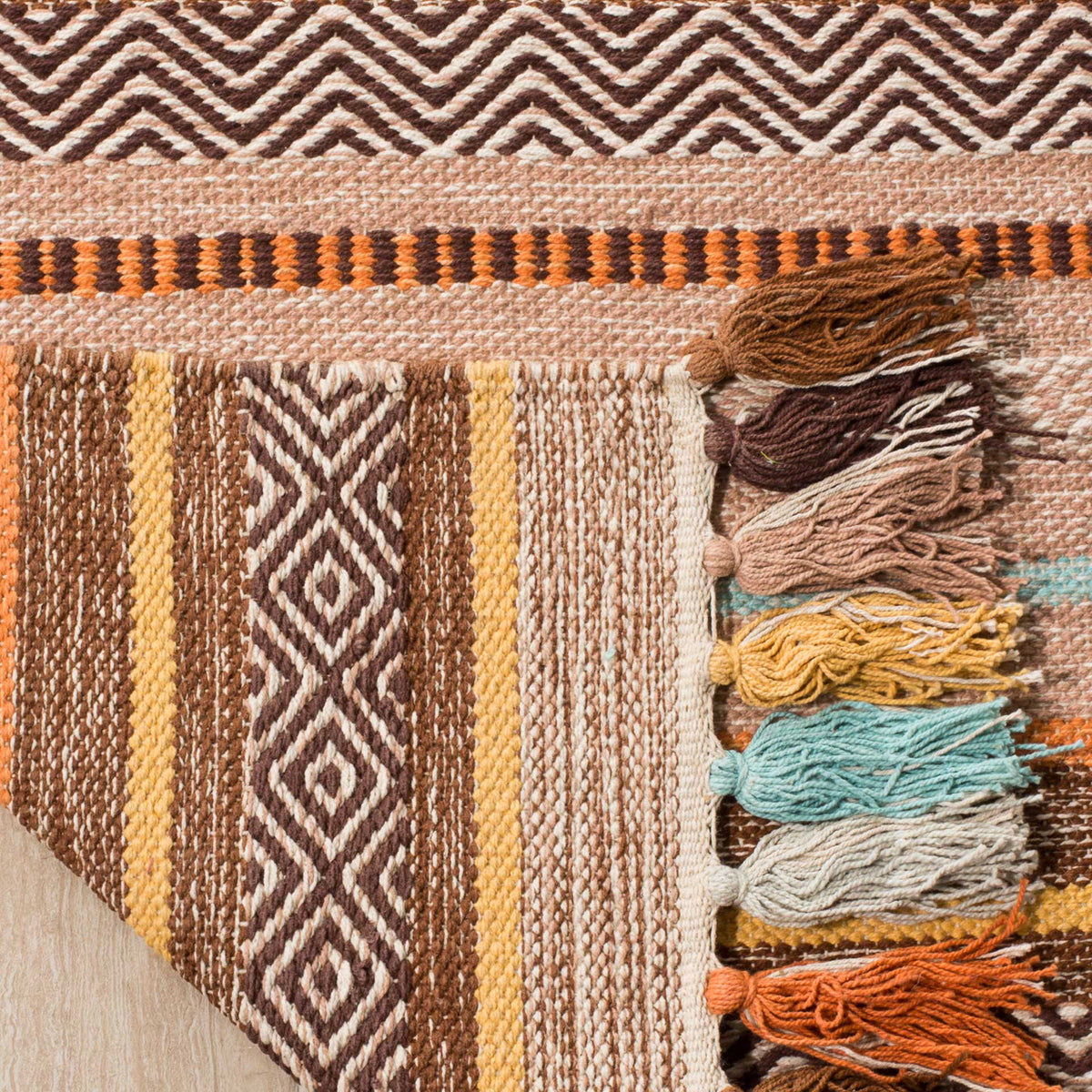 Folded corner reveals a striped cotton underside beside tassels in brown, aqua, and gold.