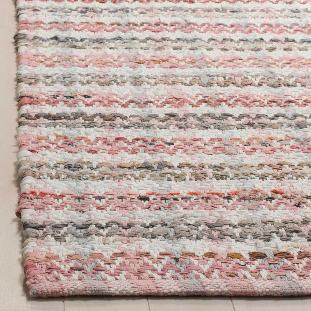 Pink, cream, and neutral cotton yarns form a tactile weave at the rug's finished corner.