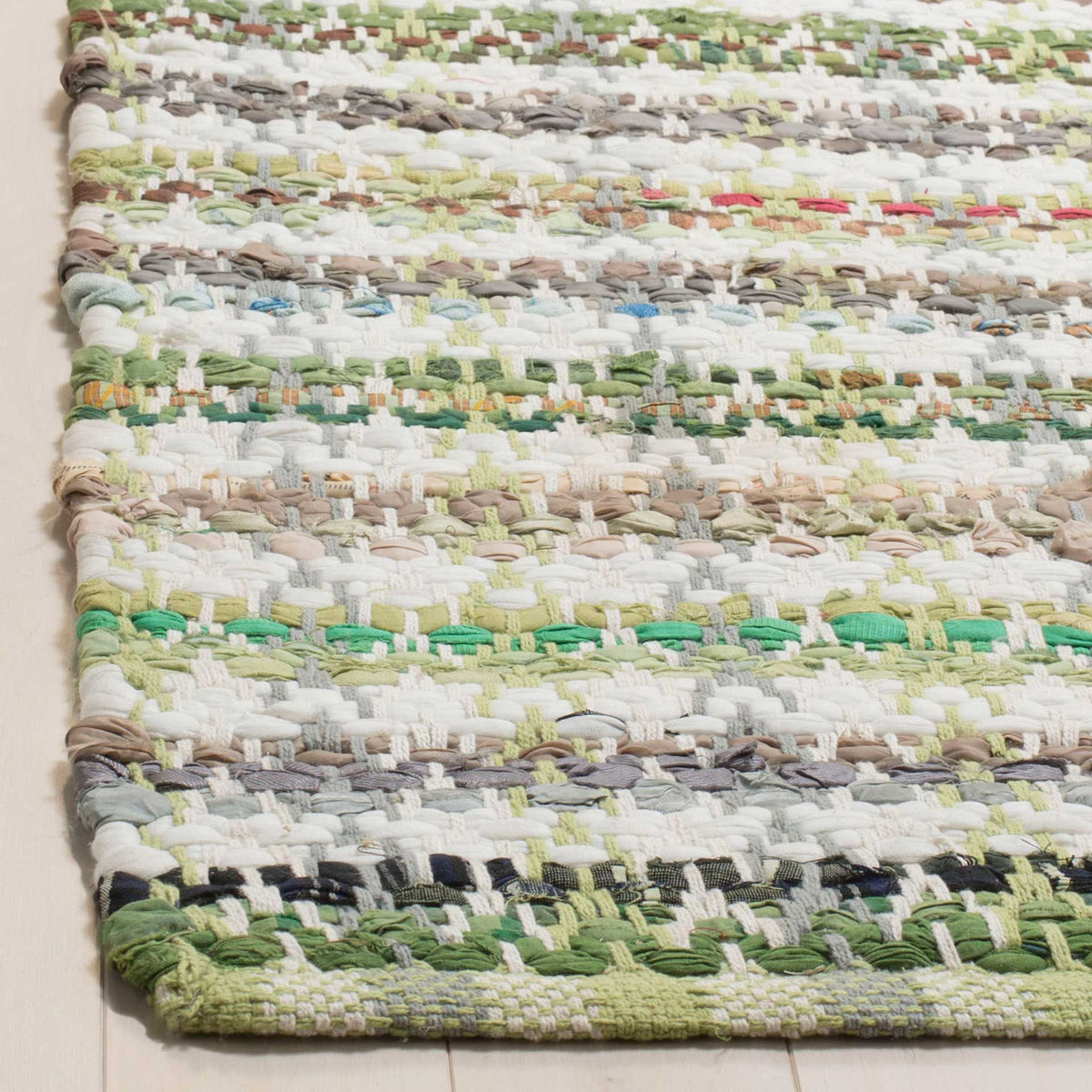 Chunky green and cream cotton yarns show rich texture along a finished rug corner.