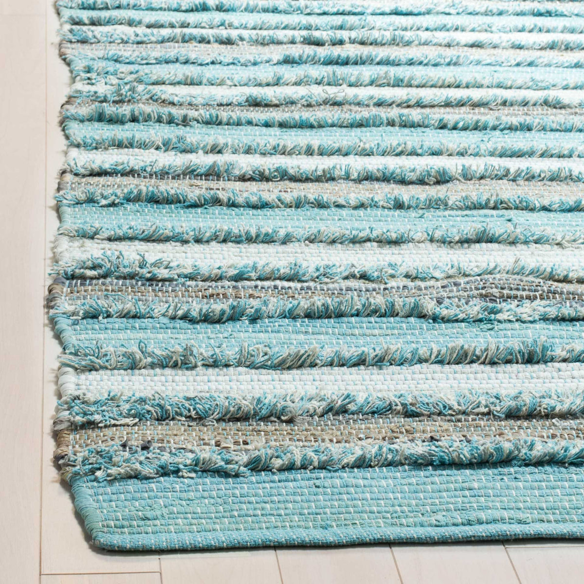 Raised aqua and white yarns meet smooth woven stripes at a neatly finished rug edge.