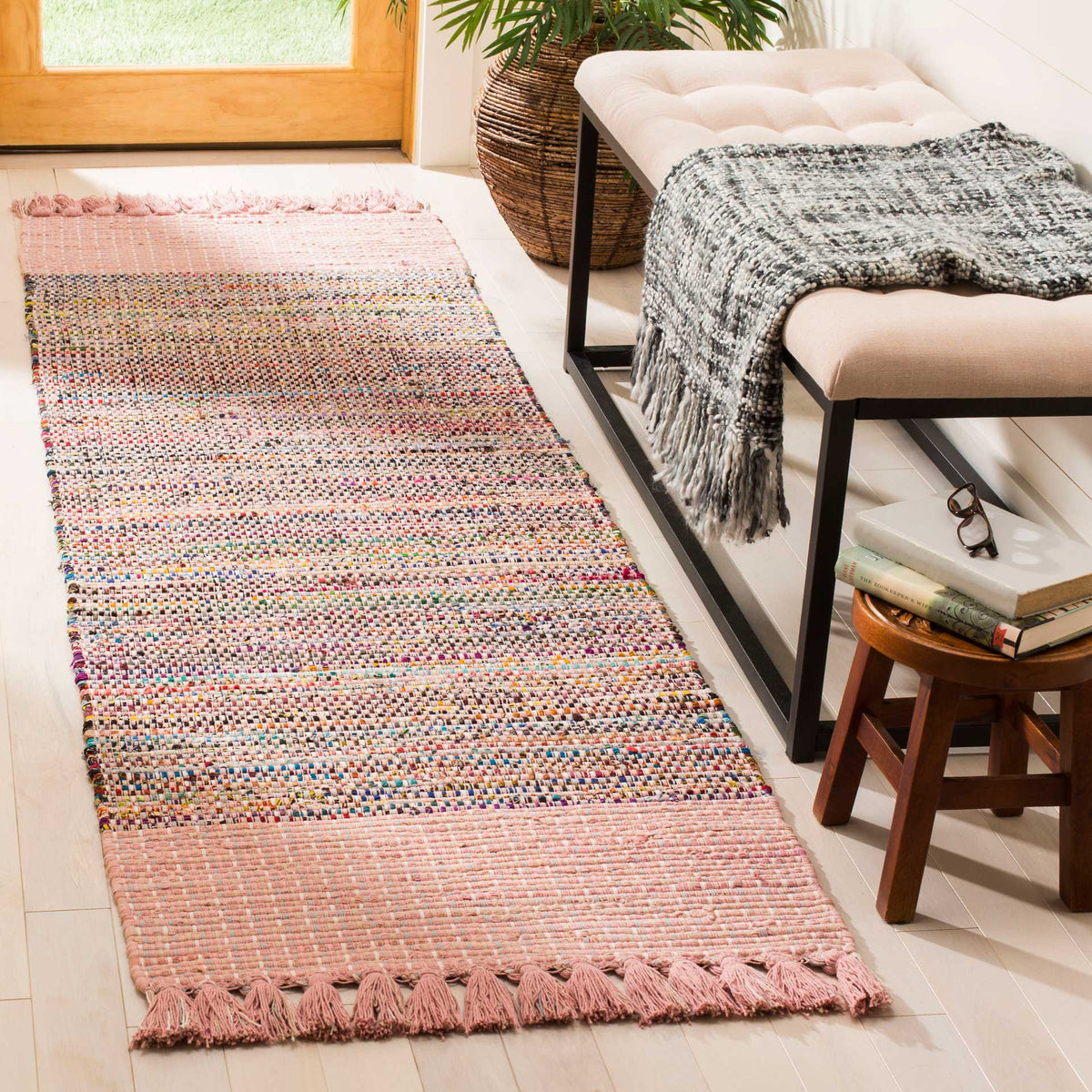 Blush pink ends and softly varied woven colors warm the floor beside a cushioned bench