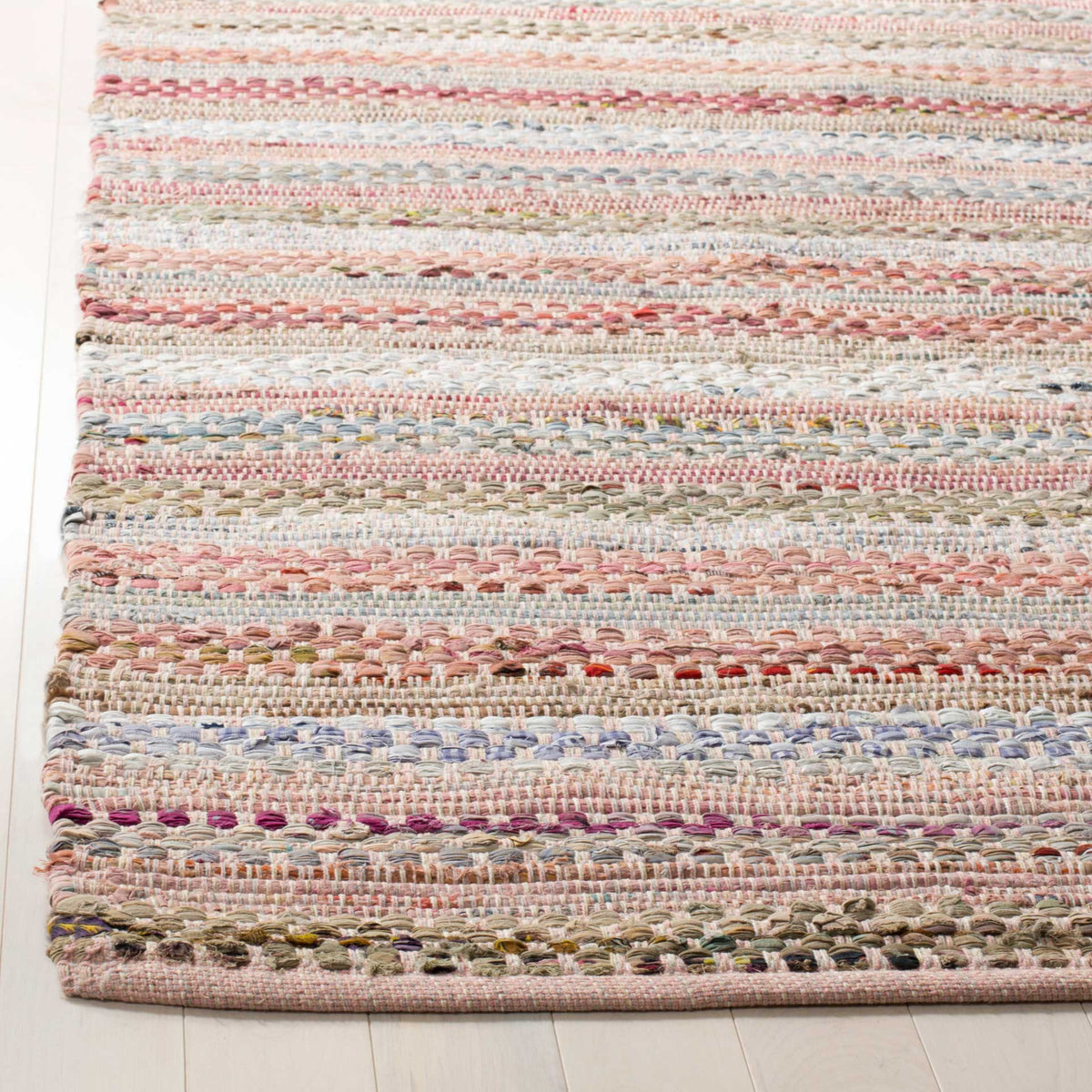 Textured pink and cream cotton threads interlace along a neatly finished rug corner.