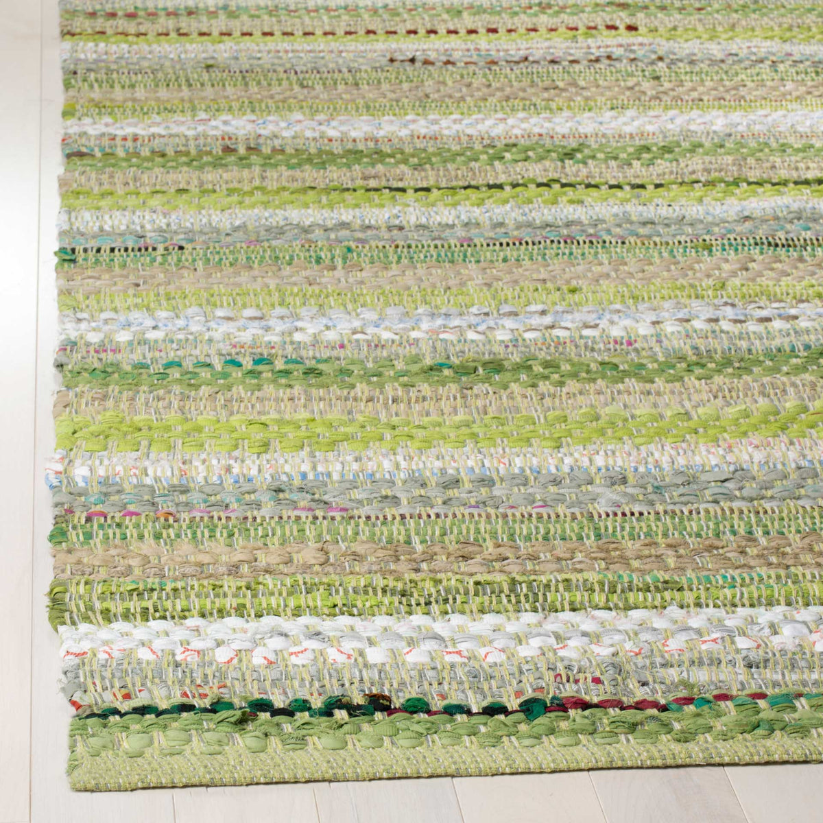 A finished rug corner shows raised green and ivory cotton yarns woven into varied stripes.