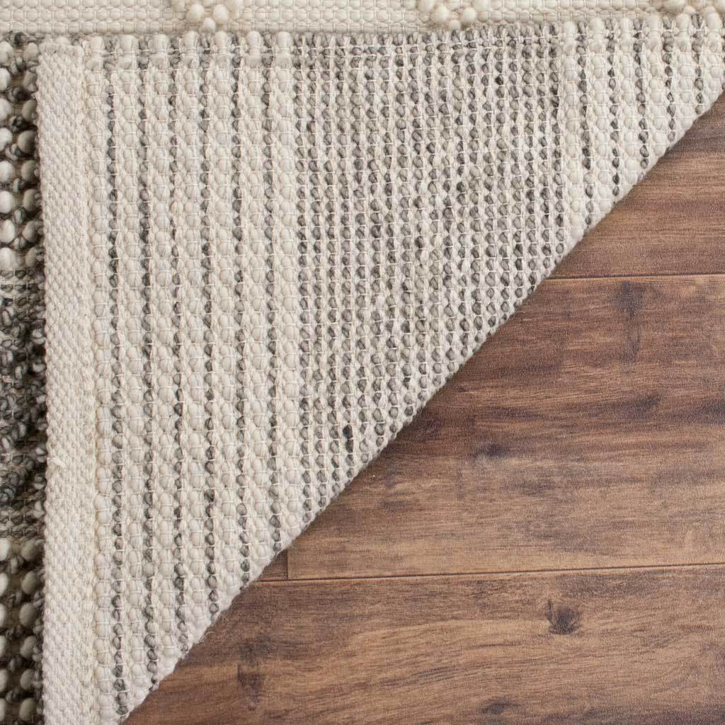 A neatly finished edge and striped gray-and-ivory backing reveal the rug's woven construction.