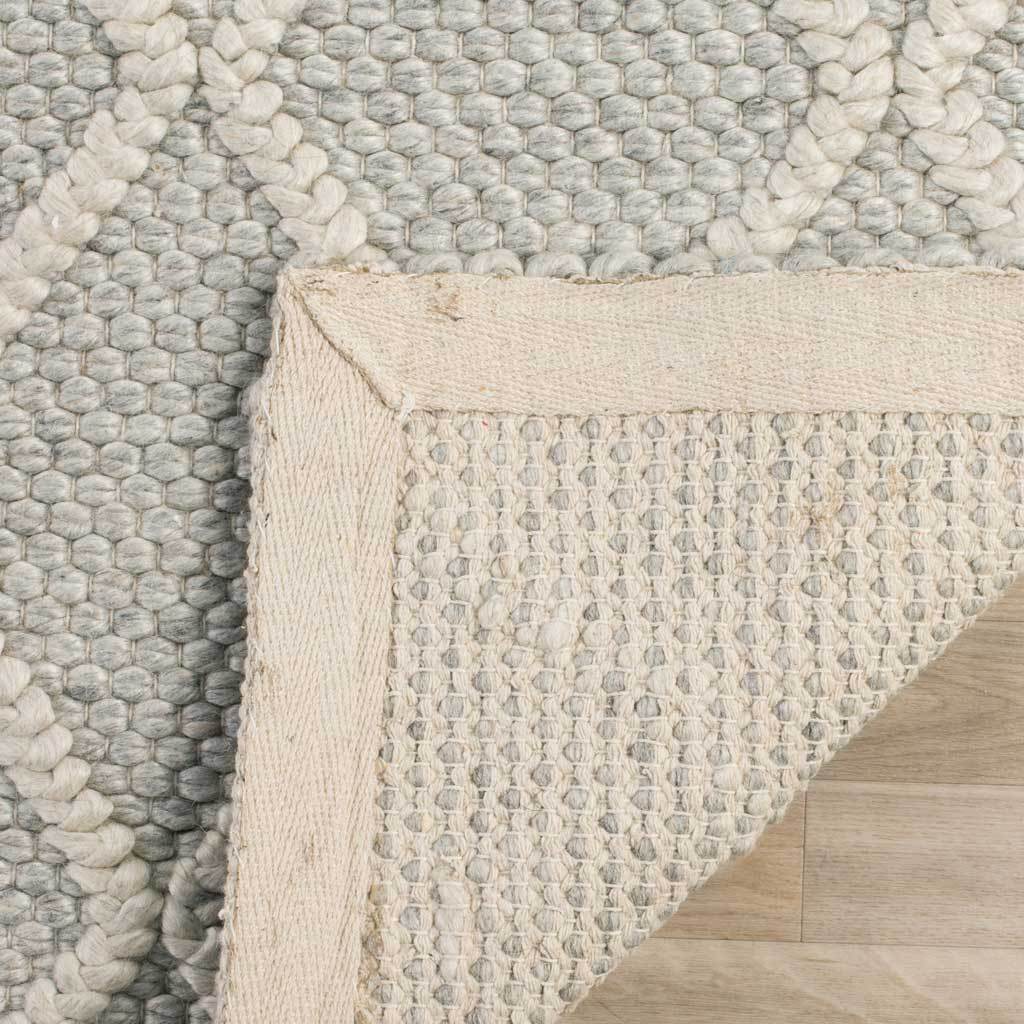 A folded edge reveals the woven underside of the silver-and-ivory diamond rug.