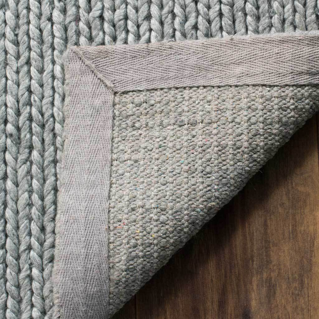A folded corner shows the steel gray rug's textured underside and reinforced fabric edge.