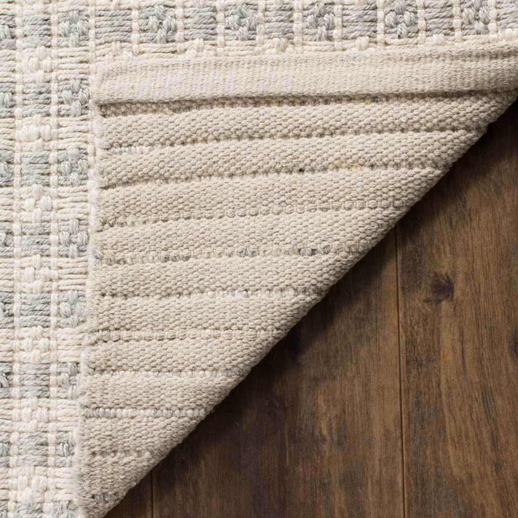 A folded edge reveals a tightly woven ivory backing beneath the rug's softly striped surface