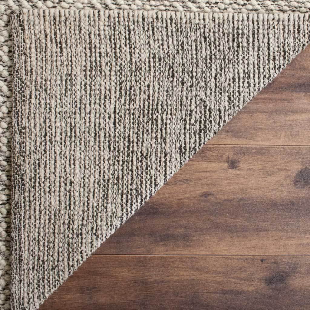A striped ivory and gray backing reveals the rug's dense weave and bound edge.