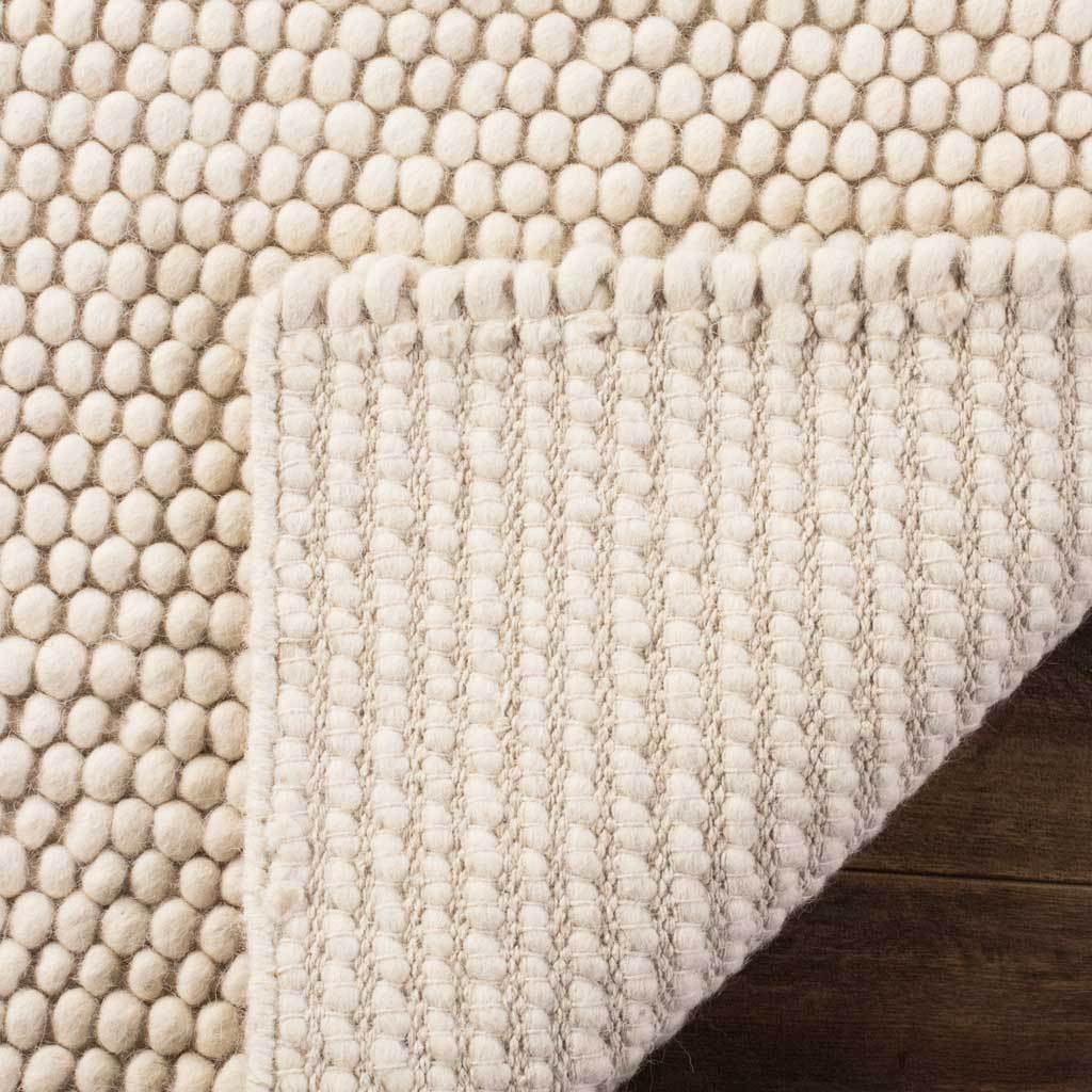 A folded edge reveals the ivory rug's woven underside beneath soft surface loops