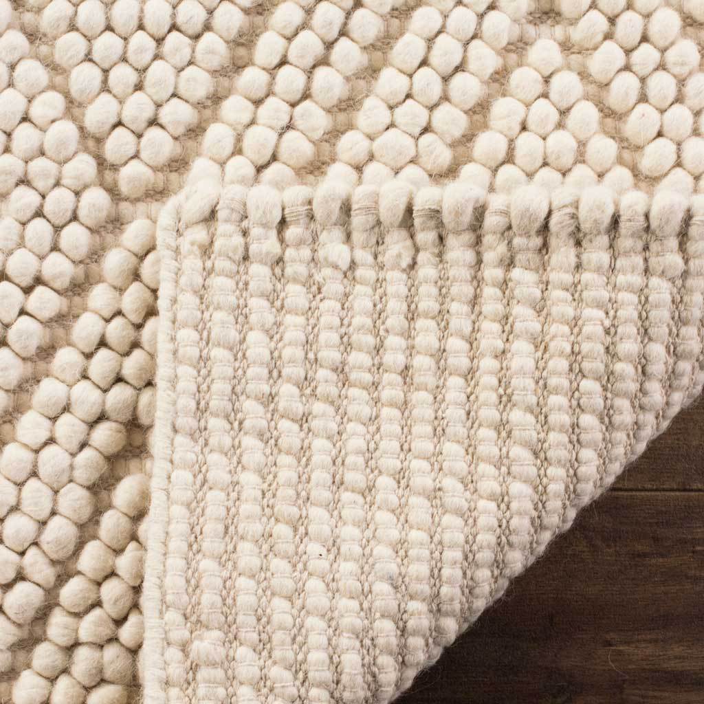 Turned-back ivory rug corner reveals a dense woven underside and a soft, looped surface