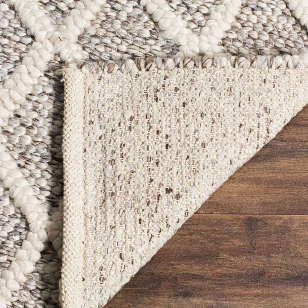 A turned-back edge reveals the woven underside beneath the rug's raised ivory lattice and stone-toned loops.