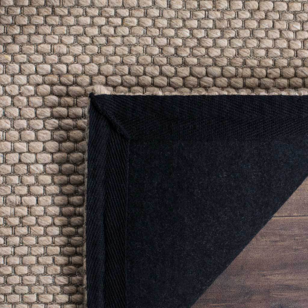 The beige rug's textured surface folds back to reveal its dark fabric backing.
