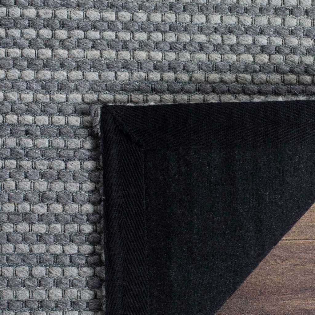 A folded corner reveals dark felt backing beneath the rug's dense gray loops.