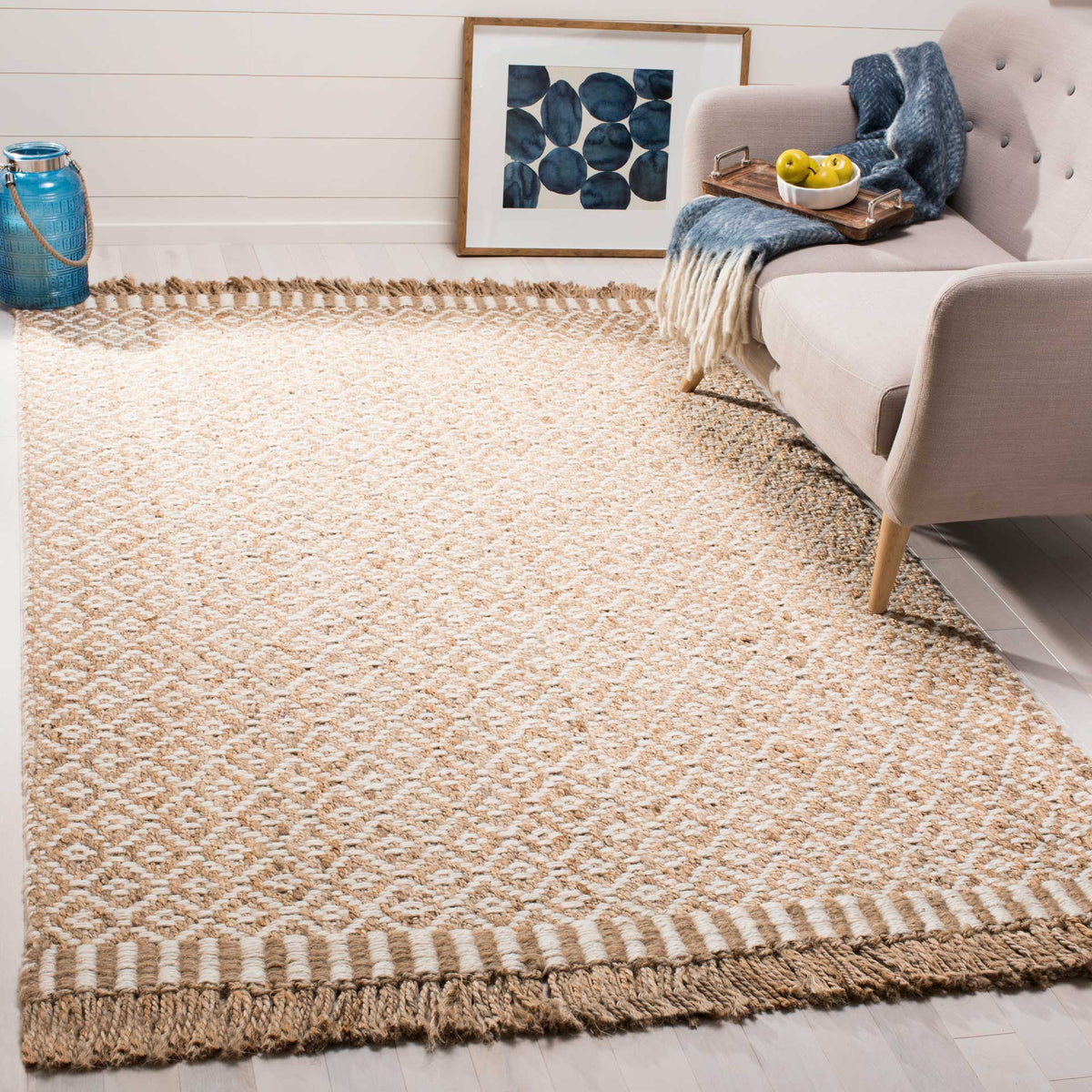 A natural jute rug with ivory diamonds and striped fringe lends texture beside a sofa.