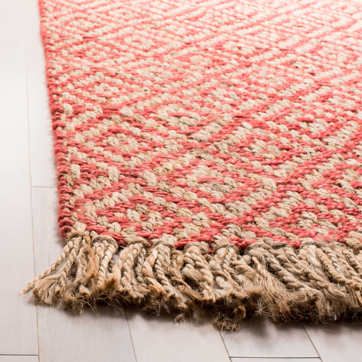 Coral-pink diamond weaving meets thick, rustic jute fringe at the rug's edge.