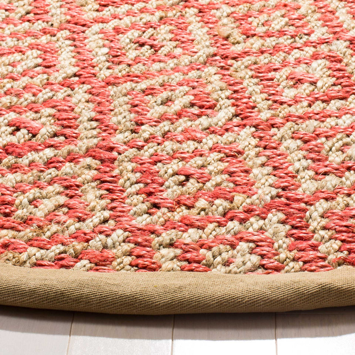 Coral-pink and natural jute yarns form raised diamond motifs beside a tan bound edge.