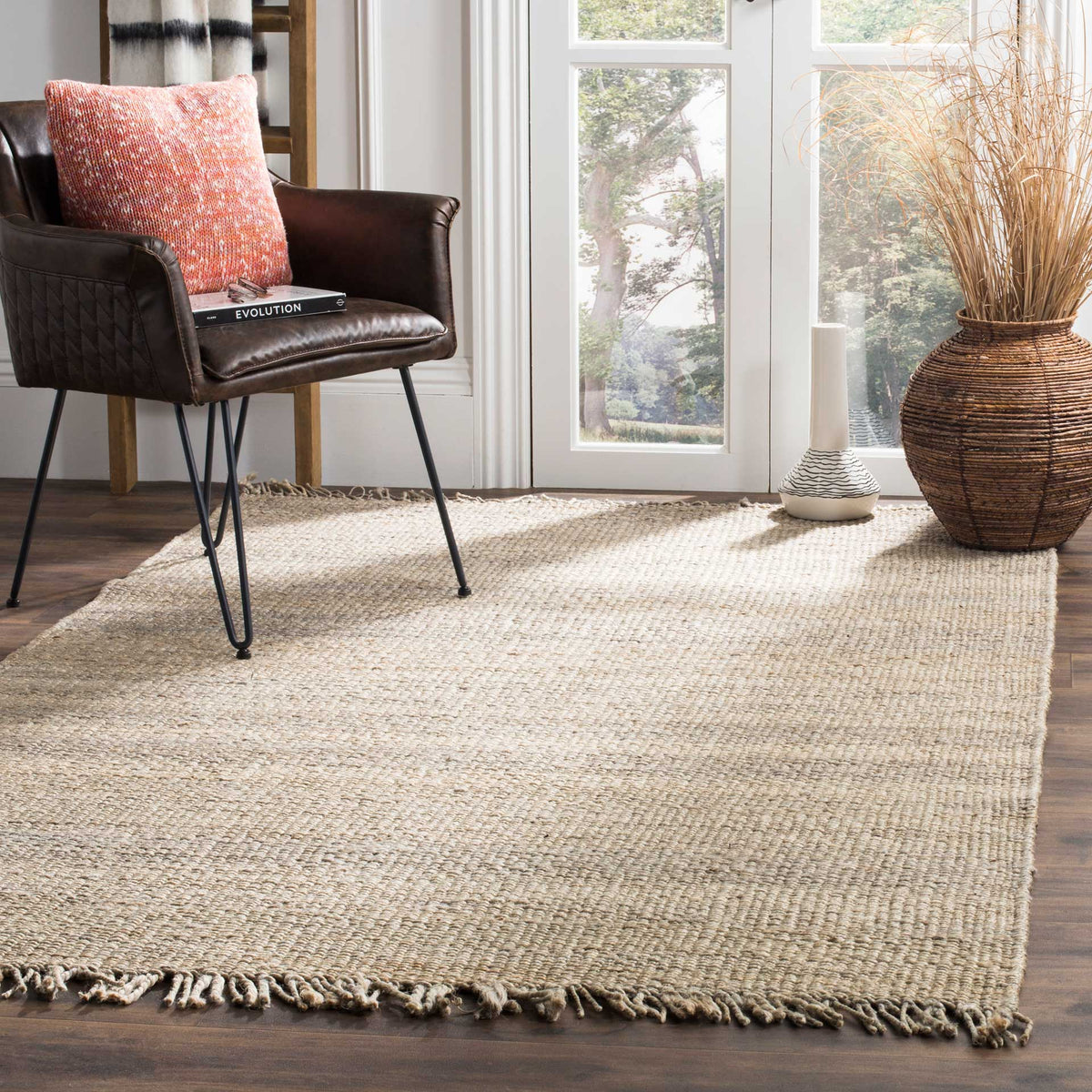 A muted gray jute rug adds rustic, fringed texture beneath a dark leather chair.
